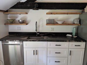 A kitchen with a dishwasher, white cabinets, black countertops, and wooden shelves. - Hay Loft Apartment in Barn - Goshen (Goshen)