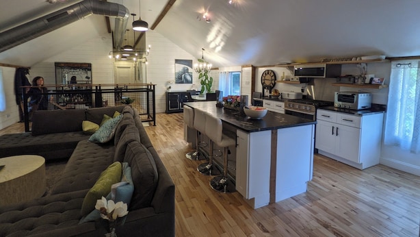 A spacious loft with a high ceiling, exposed beams, a kitchen with modern appliances, a dining area, and a living room with a large sofa. - Hay Loft Apartment in Barn - Goshen (Goshen)