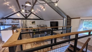 A modern kitchen with a central island, a dining area with a wooden bench, and a staircase with a metal railing. - Hay Loft Apartment in Barn - Goshen (Goshen)