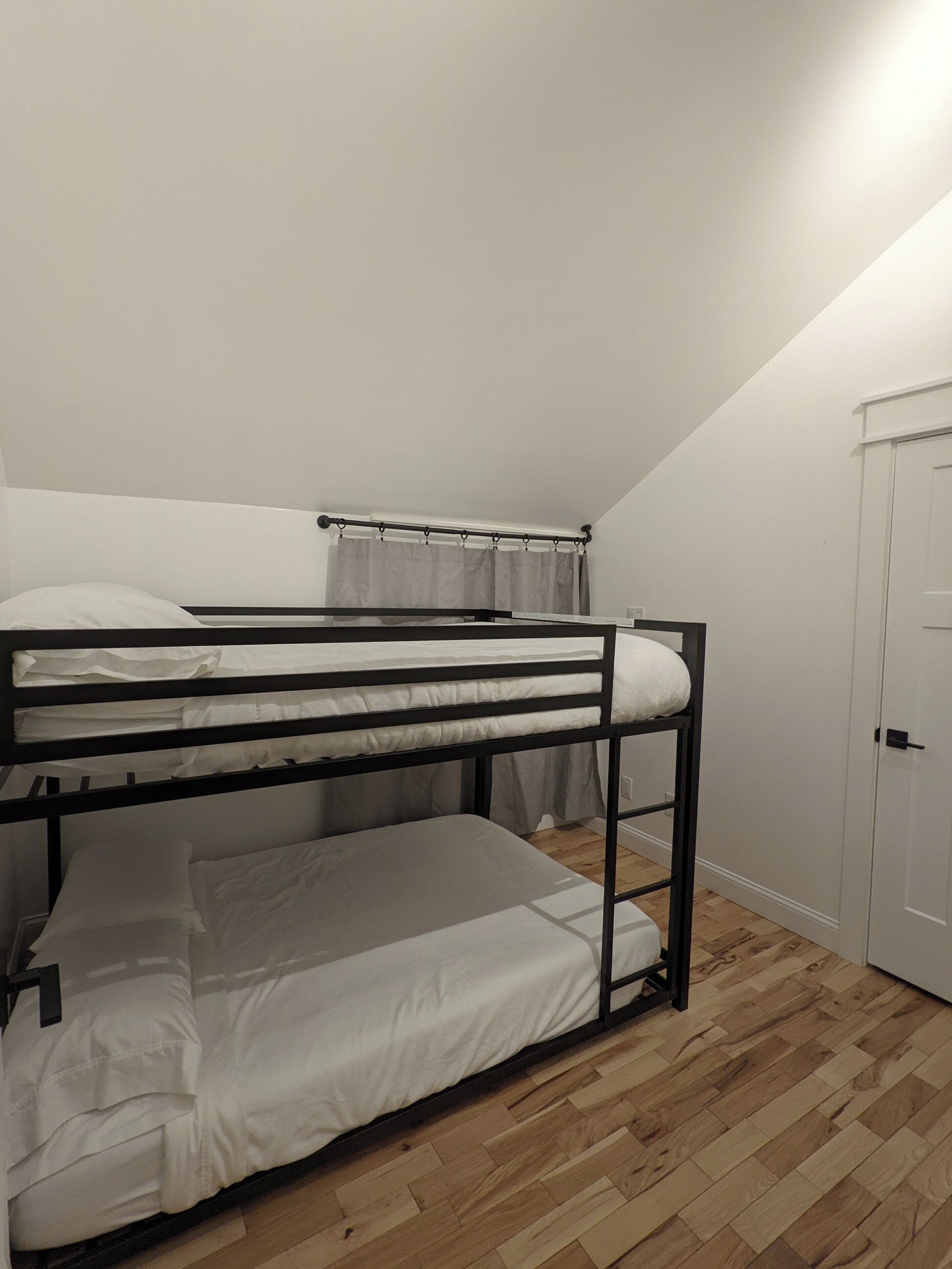 Een stapelbed in een kamer met houten vloeren, een witte deur en een gordijn.