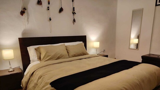 Un letto rifatto con un copriletto beige e cuscini, due abat-jour e uno specchio sulla parete.
