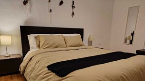 Un letto rifatto con biancheria beige, due abat-jour e uno specchio a parete.