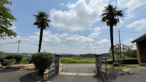 Une entrée fermée par un portail, bordée de palmiers, un ciel dégagé et une vue sur des collines lointaines.