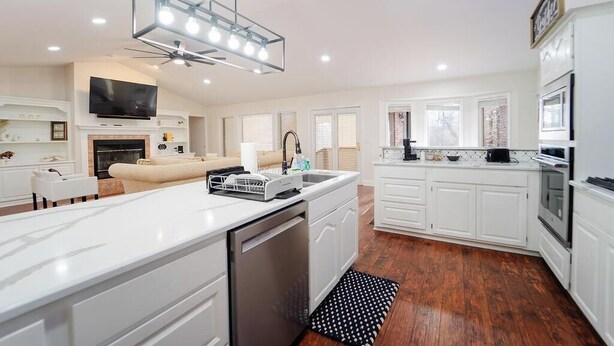 Une cuisine moderne avec des meubles blancs, un îlot central, un lave-vaisselle encastré et un luminaire au plafond.