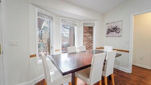 Un espace repas avec une grande table et des chaises blanches, un mur en briques et une œuvre d’art représentant une moto accrochée au mur.