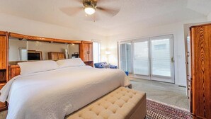 Une chambre avec un grand lit, un ventilateur de plafond, un miroir, une commode et une porte-fenêtre coulissante.