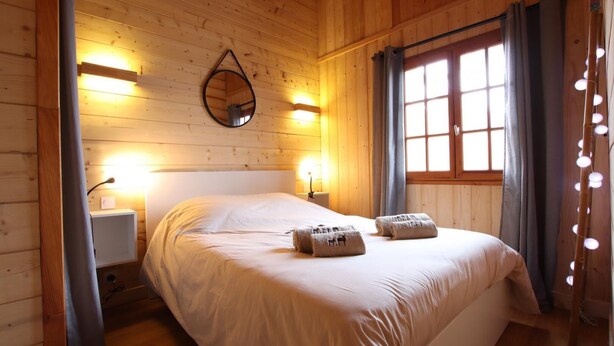 Una stanza in legno con un letto, due lampade da comodino, uno specchio e una finestra con tende.
