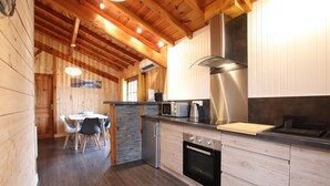 Una cucina moderna con pareti in legno, un'isola in pietra, elettrodomestici in acciaio inossidabile e un'area pranzo con tavolo e sedie.