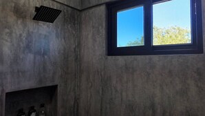 Ein Badezimmer mit großem Fenster, einer Duschbrause und einem Ablagefach mit Flaschen.