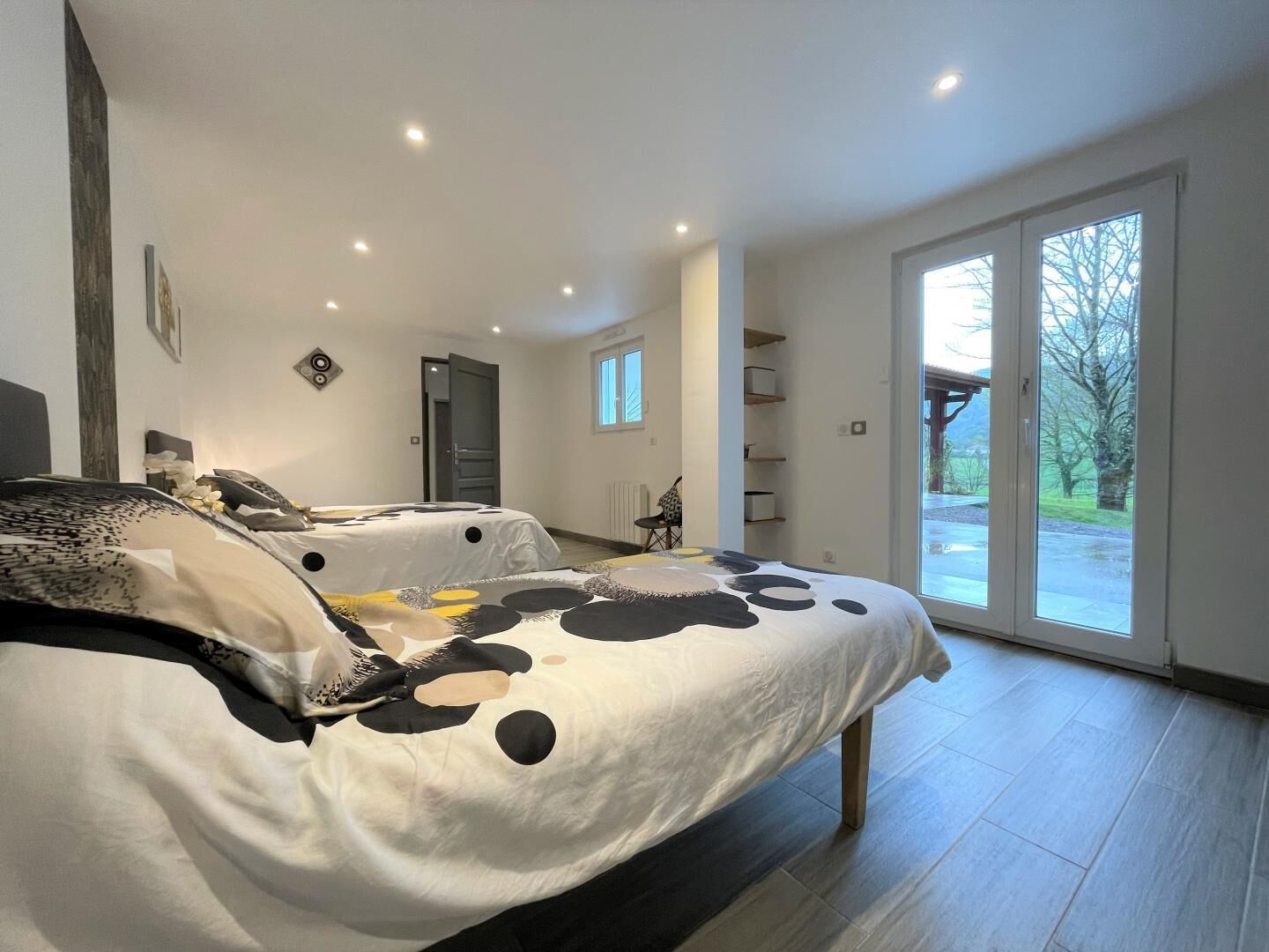 A bedroom with a large bed, a door leading to a balcony, and a view of the outdoors.