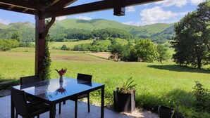 Een terras buiten met een glazen tafel en stoelen, omringd door groen en een prachtig uitzicht op glooiende heuvels.