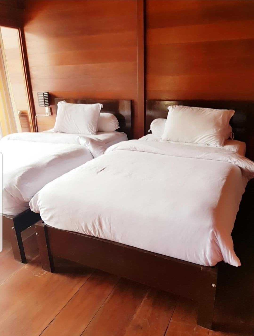 A hotel room with two beds, wooden headboards, and a wooden floor.