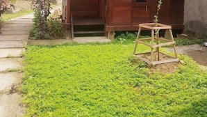 A wooden house with a tiled roof, a porch, and a small garden area with a wooden plant stand.