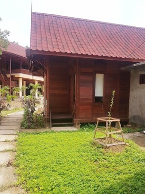 A wooden house with a tiled roof, a porch, and a small garden area with a wooden plant stand. - Korpak Villa and Resort Raja Ampat (Waisai)