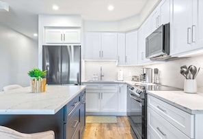 A modern kitchen with white cabinets, stainless steel appliances, and a marble countertop. - Luxury 2Bdr Beachfront Condo on Spotts Beach (Savannah)
