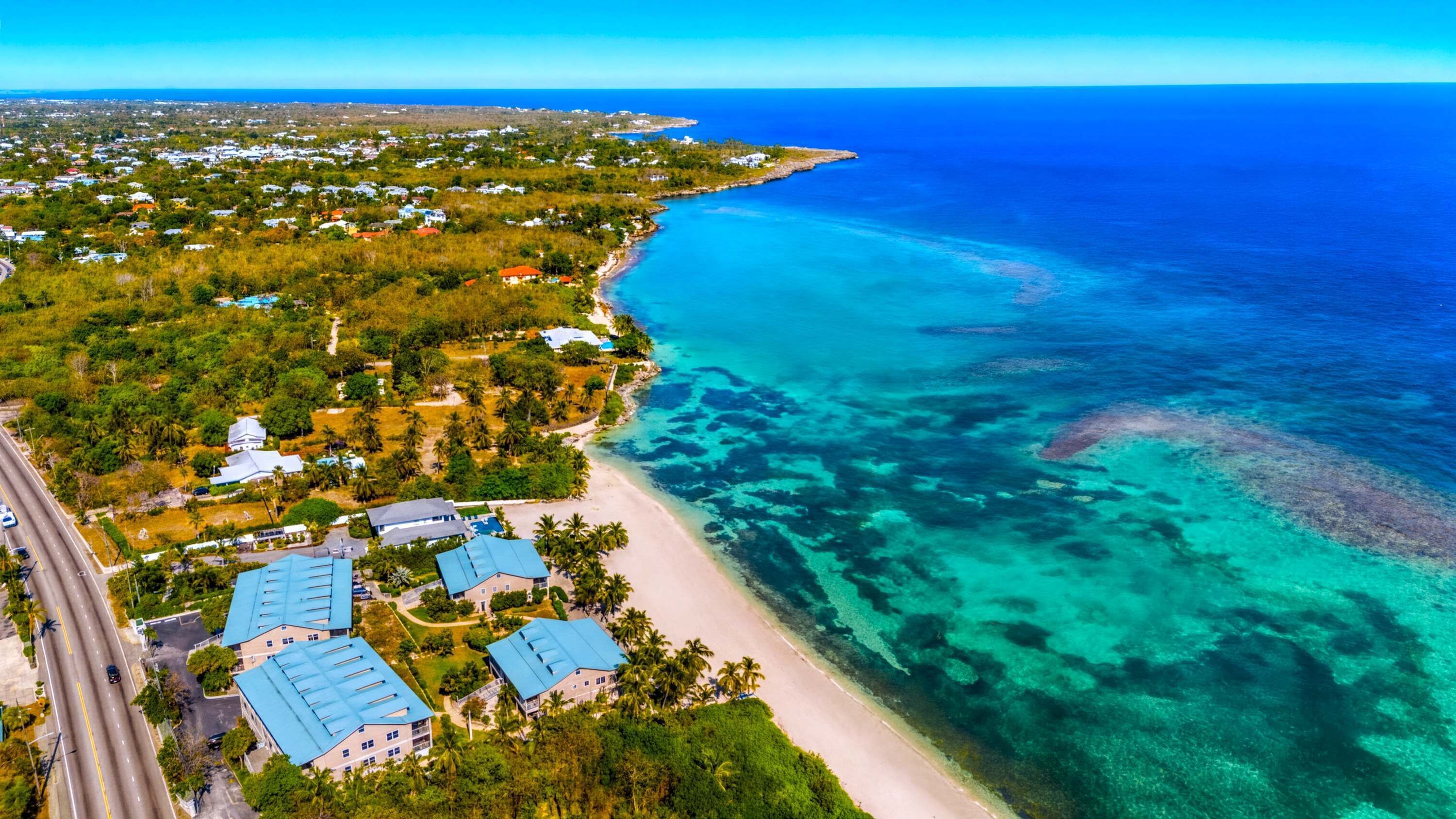 Vue aérienne d’une zone côtière avec une plage, des eaux d’un bleu limpide et des immeubles résidentiels aux toits bleus.