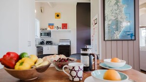 A kitchen with modern appliances, a dining table with fruit and a coffee pot, and a map of Ulladulla on the wall.