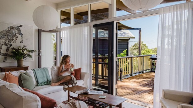 A spacious living area with a large window, a sofa, a coffee table, and a view of the outdoor deck.