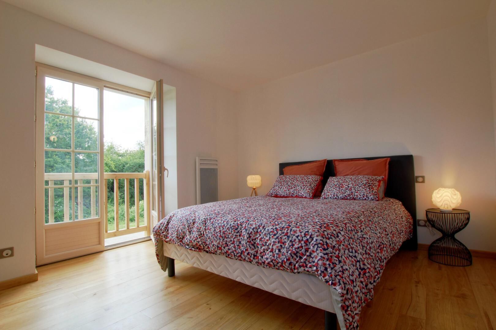 A bedroom with a bed, two bedside lamps, a window, and a balcony.