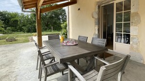 En udendørs terrasse med et træbord og stole, en stenvæg og en dør ind til huset.