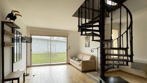 En rummelig stue med en spiraltrappe, en skydedør til en have, en sofa og et lille bord.