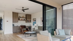 A modern living room with a sofa, armchair, and coffee table. There is a kitchen area with cabinets and a ceiling fan. - The Casita At Casa Estrella (Sedona)