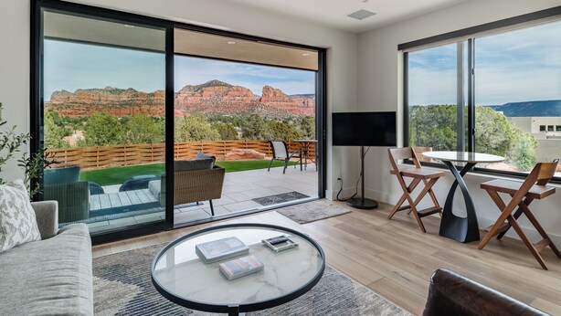 A modern living room with a large sliding glass door leading to a patio, a round coffee table, a flat-screen TV, and a dining area with wooden chairs. - The Casita At Casa Estrella (Sedona)