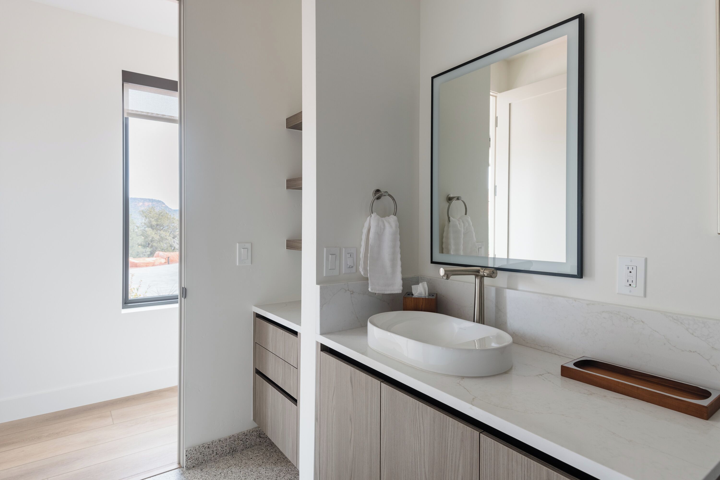 Une salle de bain moderne avec un lavabo blanc, un grand miroir et un meuble-lavabo en bois.