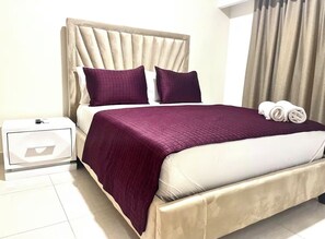 A neatly made bed with a headboard, a bedside table with a lamp, and a window with curtains. - Suite Bolivar 3bdr - Pool - Cinema -Saune - SPA (Santo Domingo)