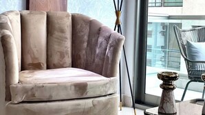 Un salon moderne avec un fauteuil moelleux, une lampe sur pied et une vue sur la ville grâce à de grandes fenêtres.