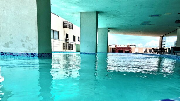 Une piscine intérieure à l'eau d'un bleu limpide, avec des bords carrelés et une vue sur les bâtiments en arrière-plan.