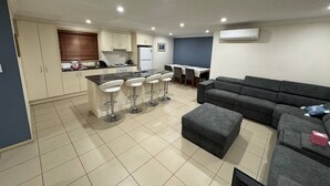 A modern kitchen with a dining area, a grey sofa, and a bar stool set.