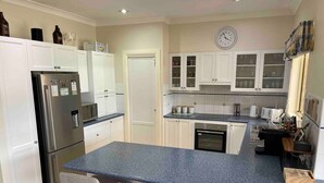 A modern kitchen with white cabinets, a stainless steel refrigerator, a built-in oven, and a large island with bar stools. - Resort style villa with pool “Rest Easy Mudgee” (Mudgee)