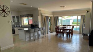 A spacious kitchen with a central island, a dining area with wooden chairs, and large windows with curtains. - Resort style villa with pool “Rest Easy Mudgee” (Mudgee)