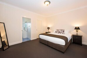 A bedroom with a large bed, two bedside tables with lamps, a mirror, and a door leading to a bathroom. - Resort style villa with pool “Rest Easy Mudgee” (Mudgee)