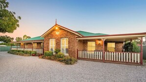 A two-story brick house with a green roof, a porch with a white picket fence, and a gravel driveway. - Resort style villa with pool “Rest Easy Mudgee” (Mudgee)