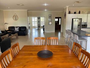 A spacious living area with a wooden dining table and chairs, a sofa, and a kitchen with white cabinets and a refrigerator.
