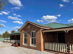 A brick building with a green roof, a porch, and a gravel driveway. - Resort style villa with pool “Rest Easy Mudgee” (Mudgee)