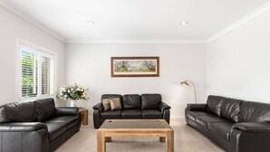 A modern living room with two black leather sofas, a wooden coffee table, and a framed landscape painting on the wall. - Resort style villa with pool “Rest Easy Mudgee” (Mudgee)