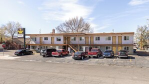 Um motel de dois andares com estacionamento, uma placa de pare e um céu claro.