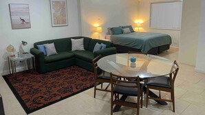 A compact living space with a green sofa, a dining table with chairs, a small side table, and a bed with a green cover. - Spacious & comfy studio unit “Rest Easy Mudgee” (Mudgee)