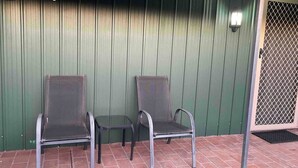 Two metal chairs with armrests and a small table, placed on a brick patio against a green corrugated metal wall. - Spacious & comfy studio unit “Rest Easy Mudgee” (Mudgee)