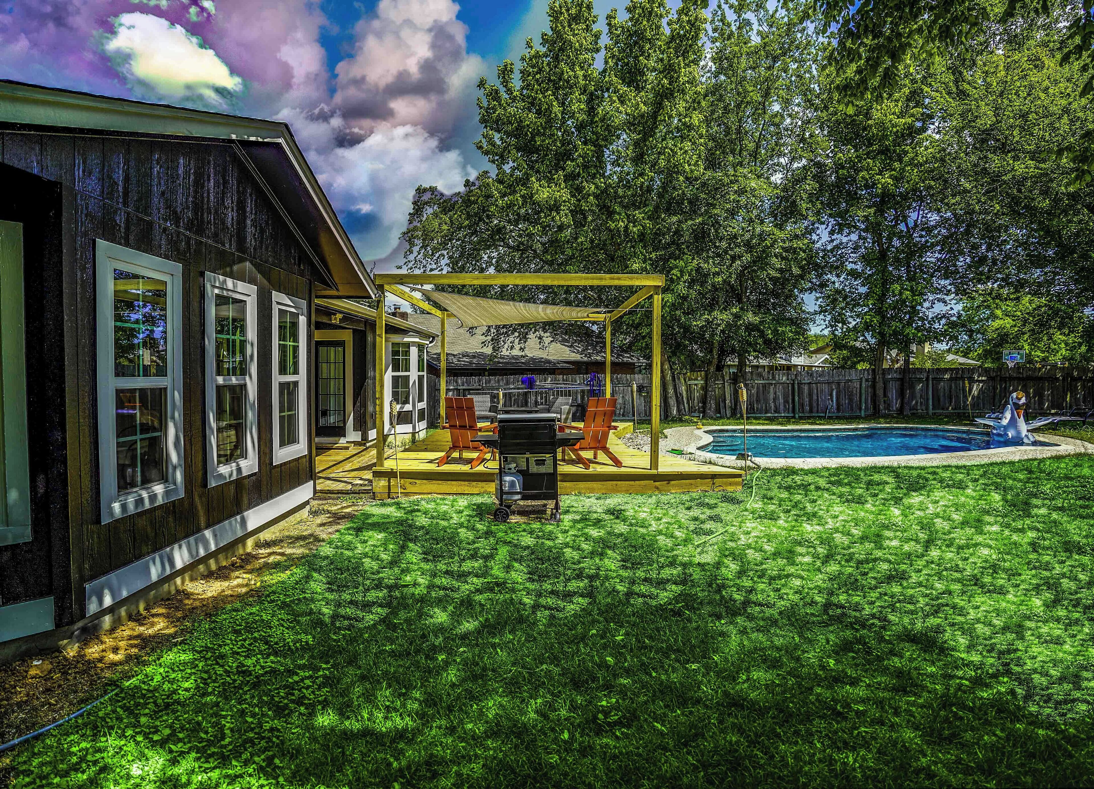 A backyard with a wooden deck, a barbecue area, a swimming pool, and a fenced yard.