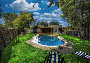 Ein Garten mit Swimmingpool, einer Holzterrasse und einem Haus im Hintergrund.