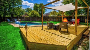 Ett trädäck med ett takförsett sittområde, en pool och en grill.