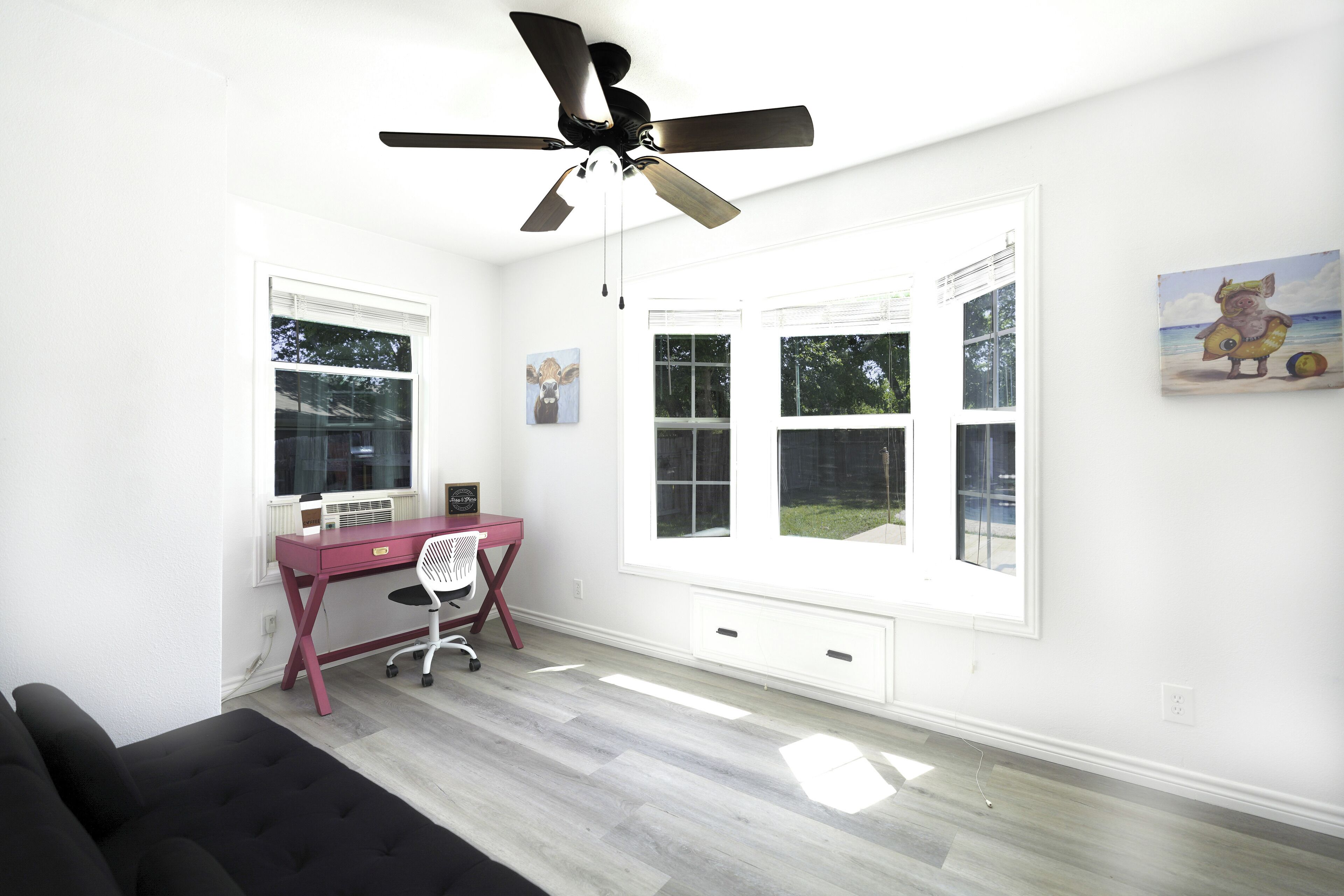 A bright room with a desk, chair, and a ceiling fan.