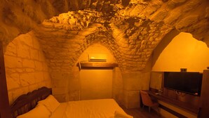 Una habitación con pared de piedra, cama con ropa blanca, televisor de pantalla plana y escritorio de madera.