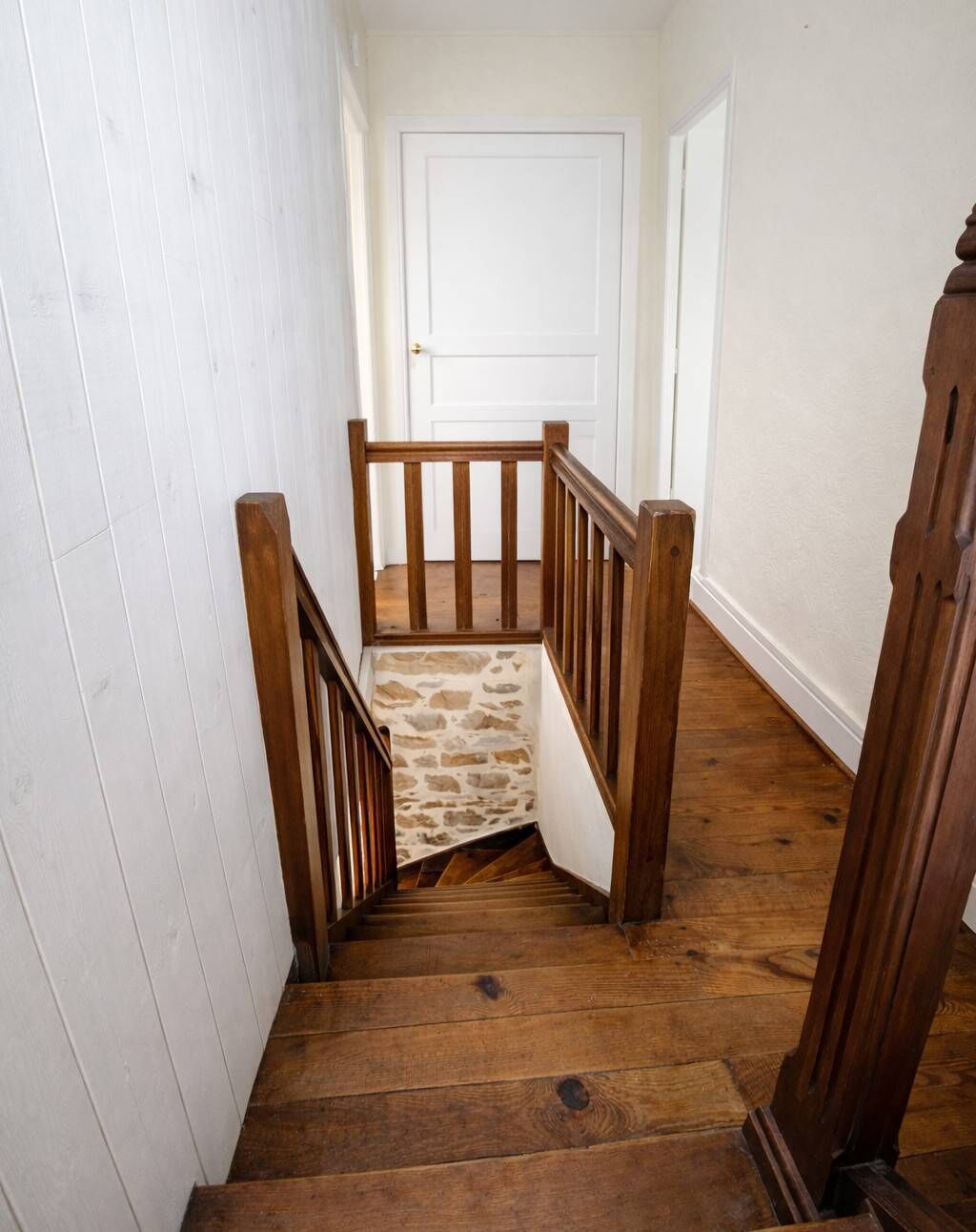 A wooden staircase with a stone accent wall, white walls, and a white door at the top.