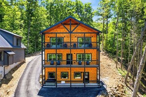 A multi-story log cabin with a symmetrical design, featuring a central balcony and multiple windows on each floor. - 6BR Smoky Mtn · Indoor Pool ·Sleeps 18· Dollywood (Sevierville)
