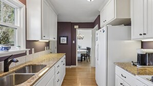 Eine Küche mit weißen Schränken, Granit Arbeitsplatten, einer Spüle und einem Kühlschrank.